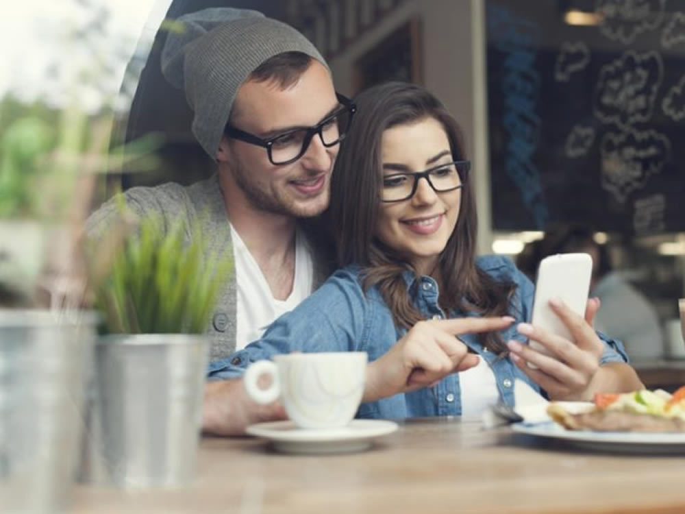 Smiling young couple look up the six Cs of success for cash and couples on her phone