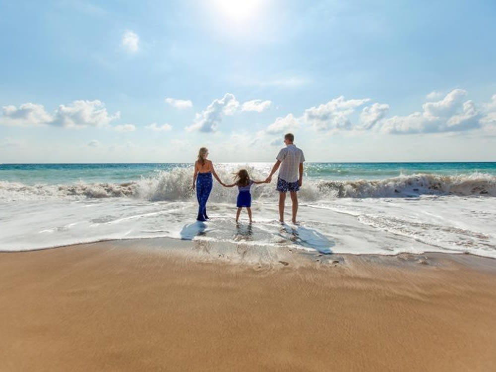 Couple and young daughter stand in the surf and save money on vacations