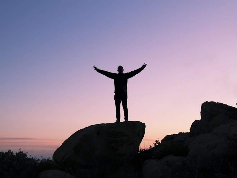 Man on mountaintop symbolizes financial success from maxing your 401(k)